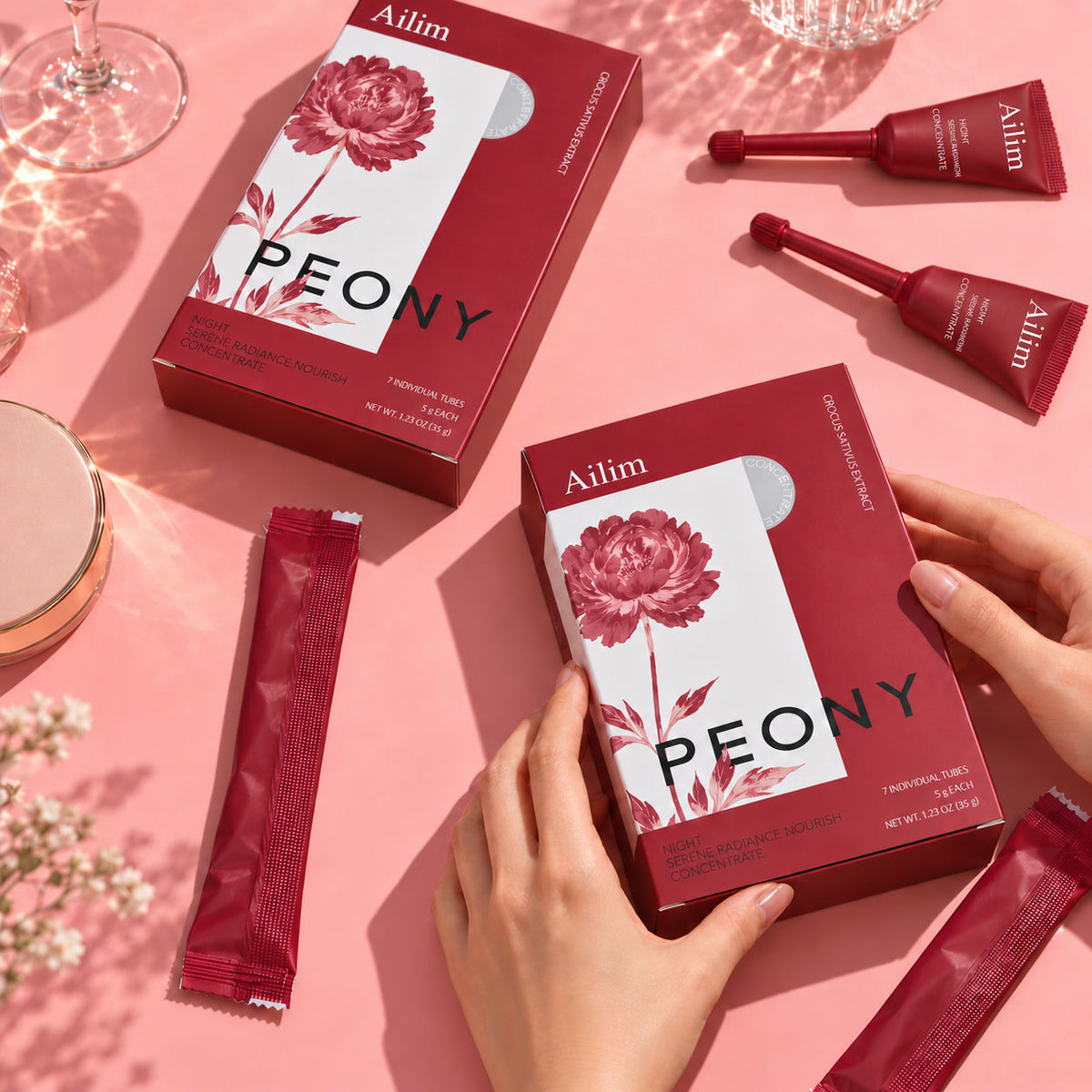 Hands holding an Ailim Peony box, with applicator tubes and individual sachets on a pink tabletop.
